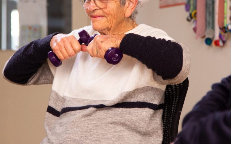 Elderly woman sitting in chair using hand weights