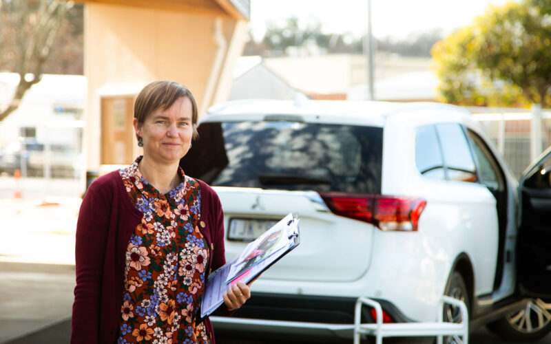 Woman holding clipboard standing outside behind car